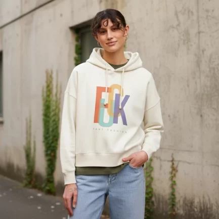 Women wearing hoodie with print: Fuck Fast Fashion in front of a concrete wall
